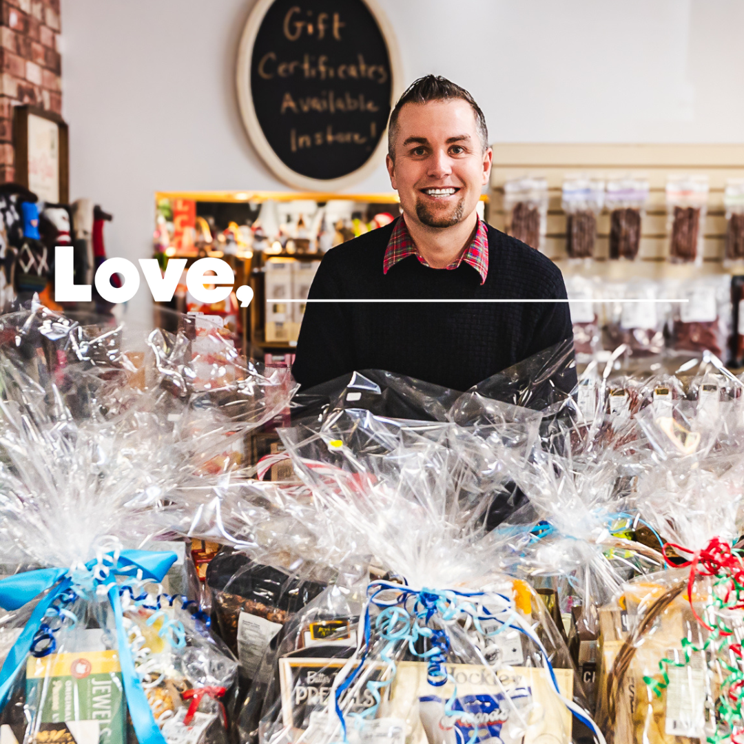 A smiling man in a black shirt stands behind a stack of gift backets in a shop.